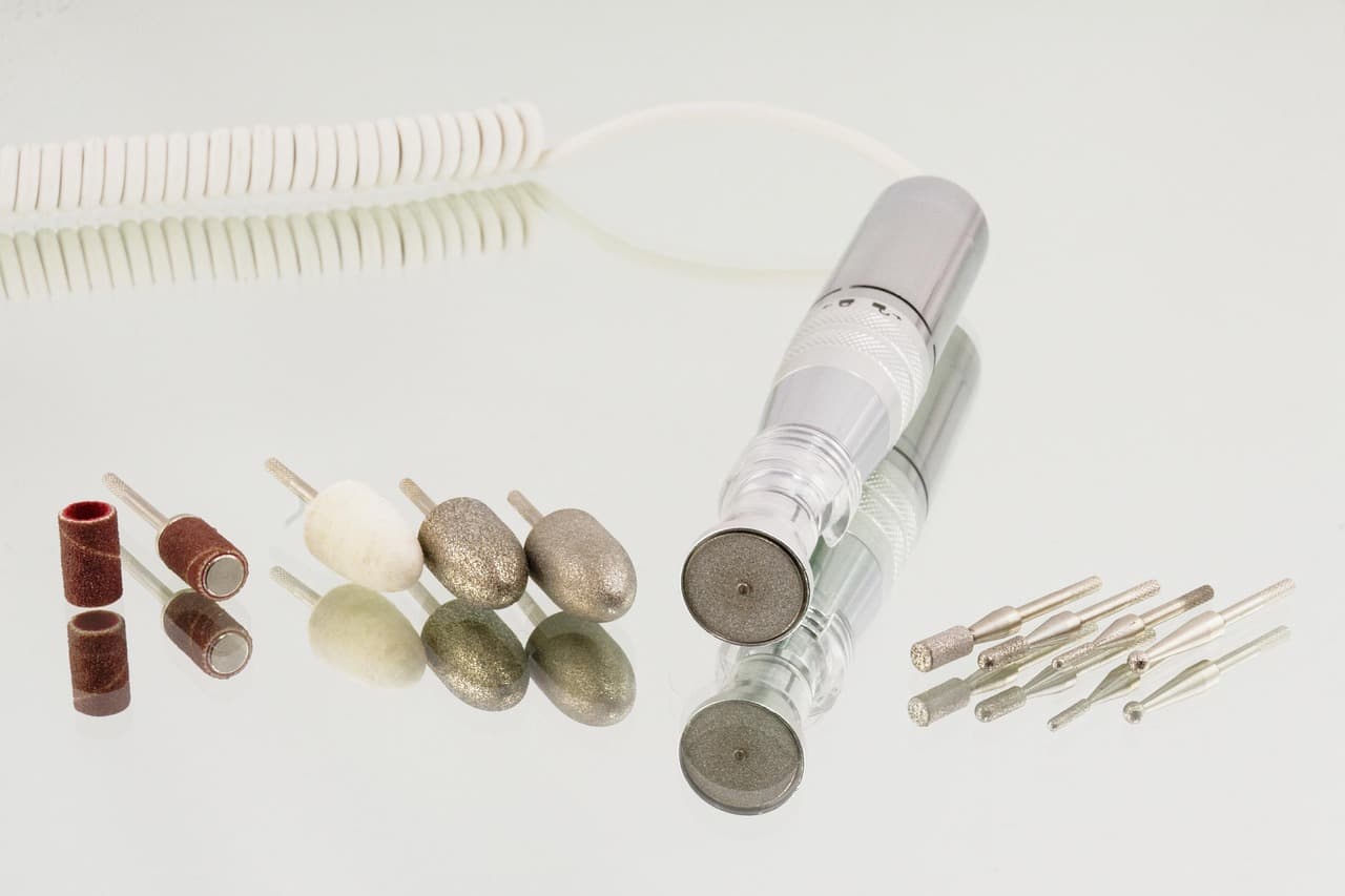 A nail drill and a row of clean bits and sanding bands laid out on a white mirror
